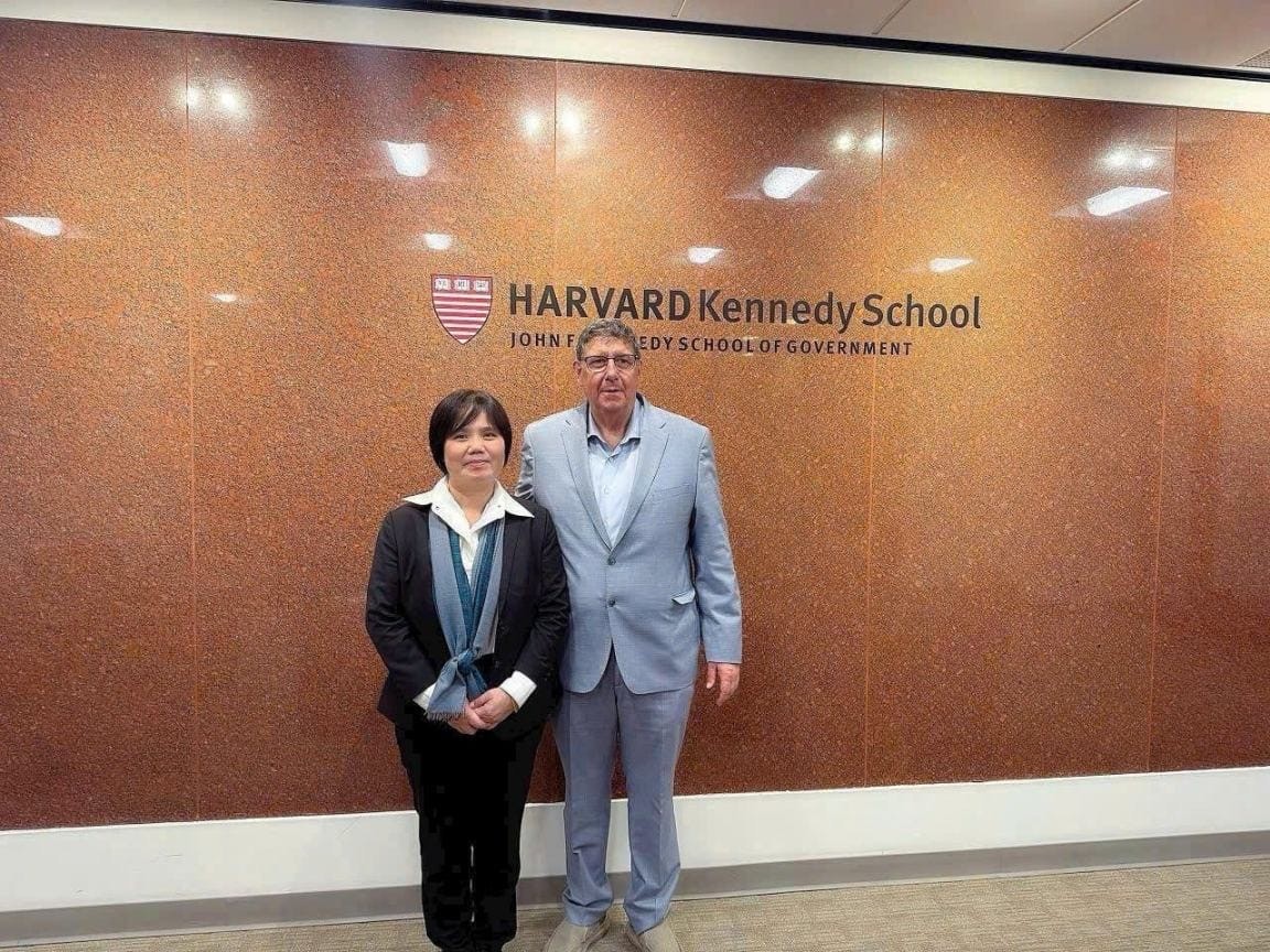 Two visitors standing in front of the Harvard Kennedy School sign